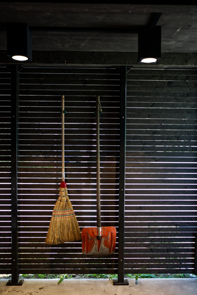 Inneraum von Pavillon, ein Besen und eine Schaufel hängen an der Holzschalung